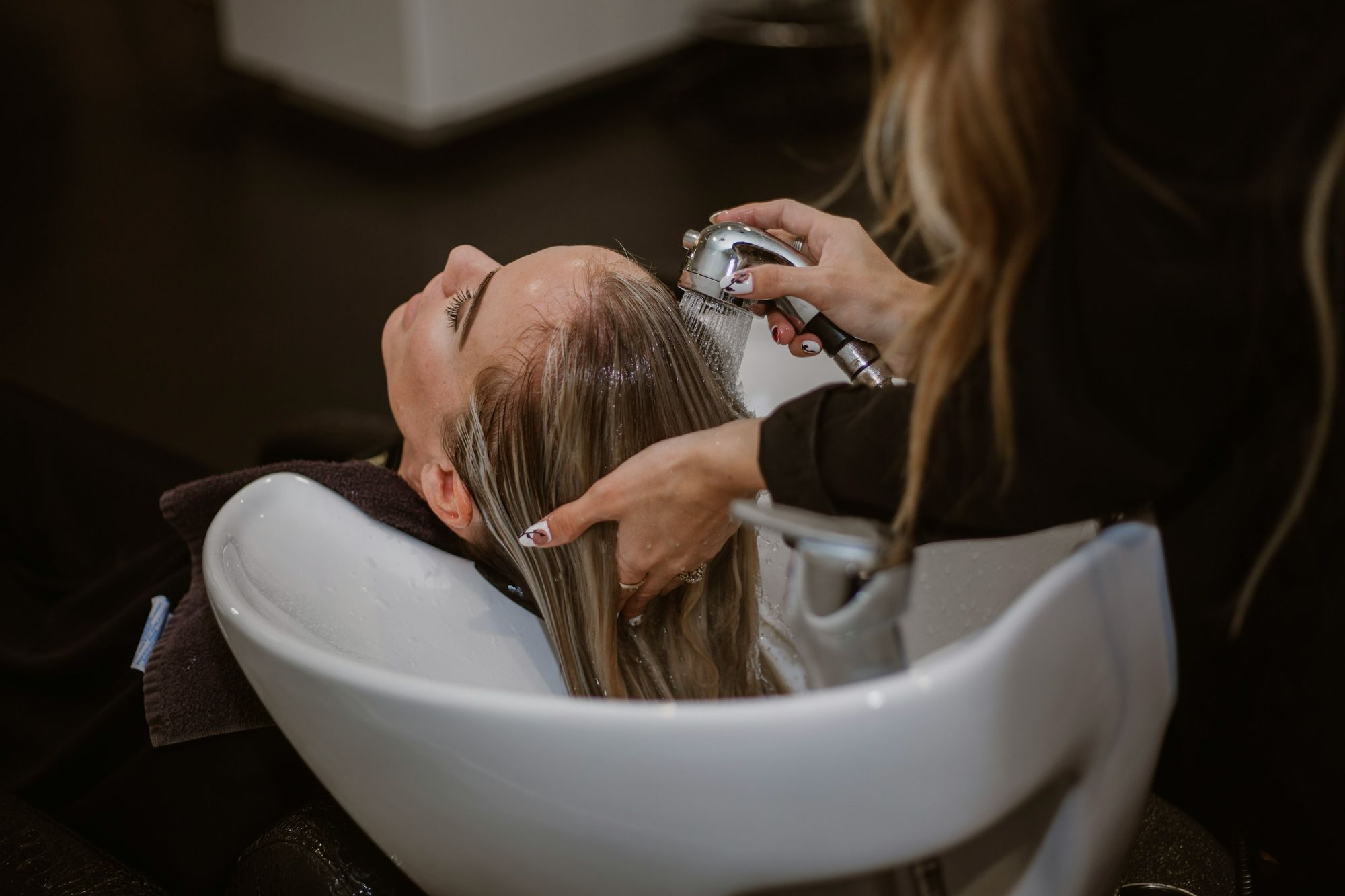 A person is getting a hair wash at a salon, with a stylist rinsing their hair over a sink.