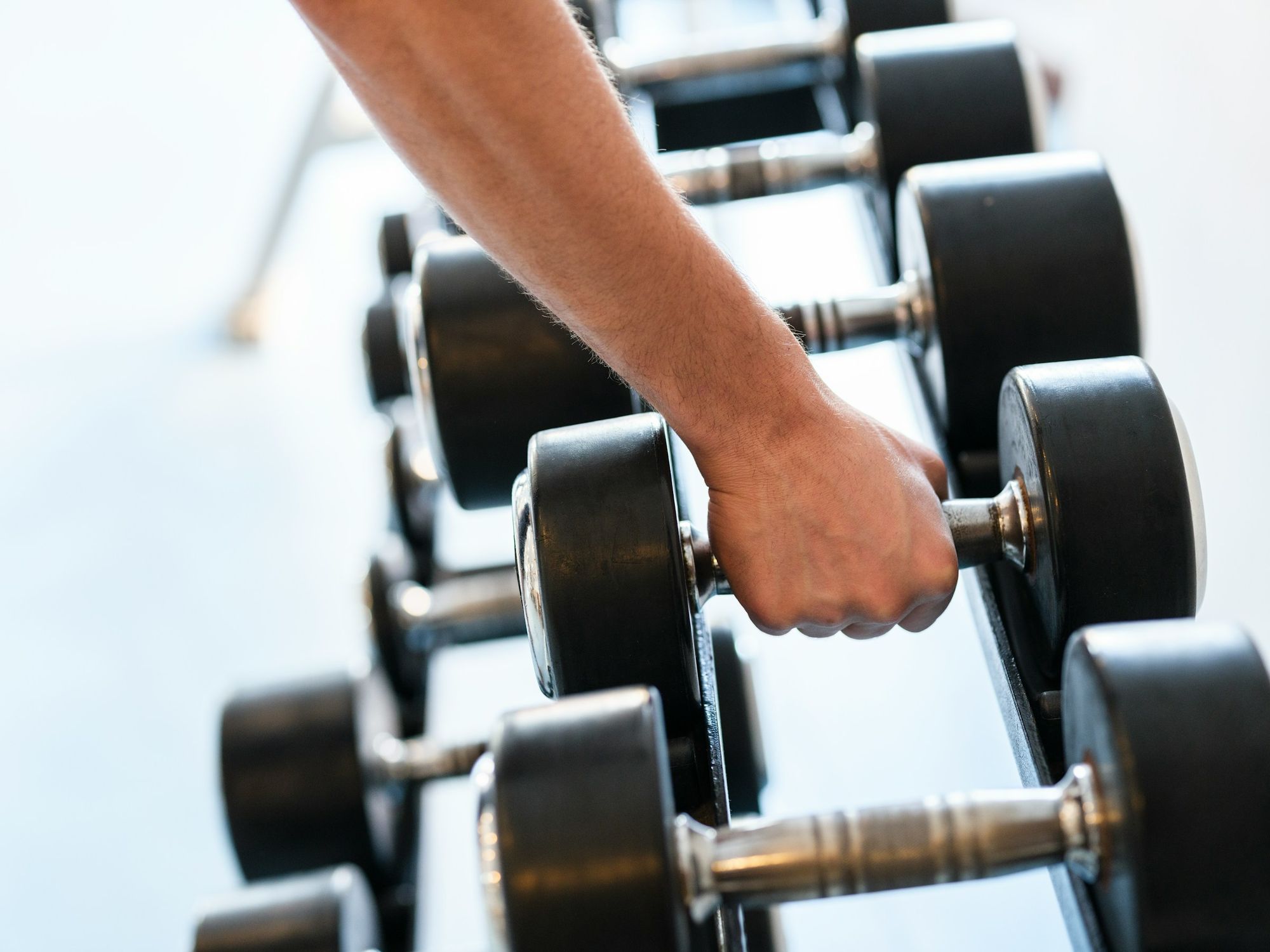 A person gripping a dumbbell in a gym, with row of free weights lined up on a rack near them.