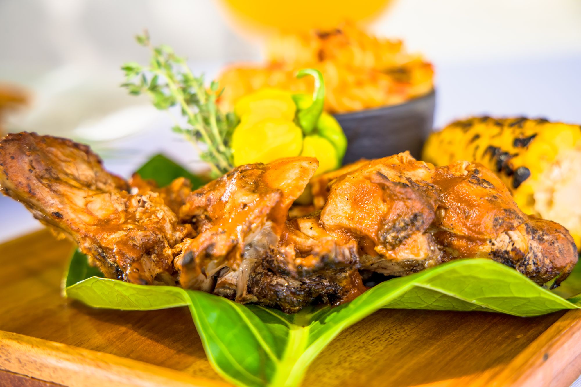 Grilled pieces of meat on a wooden board, topped with yellow sauce, herbs, and green leafy garnish.