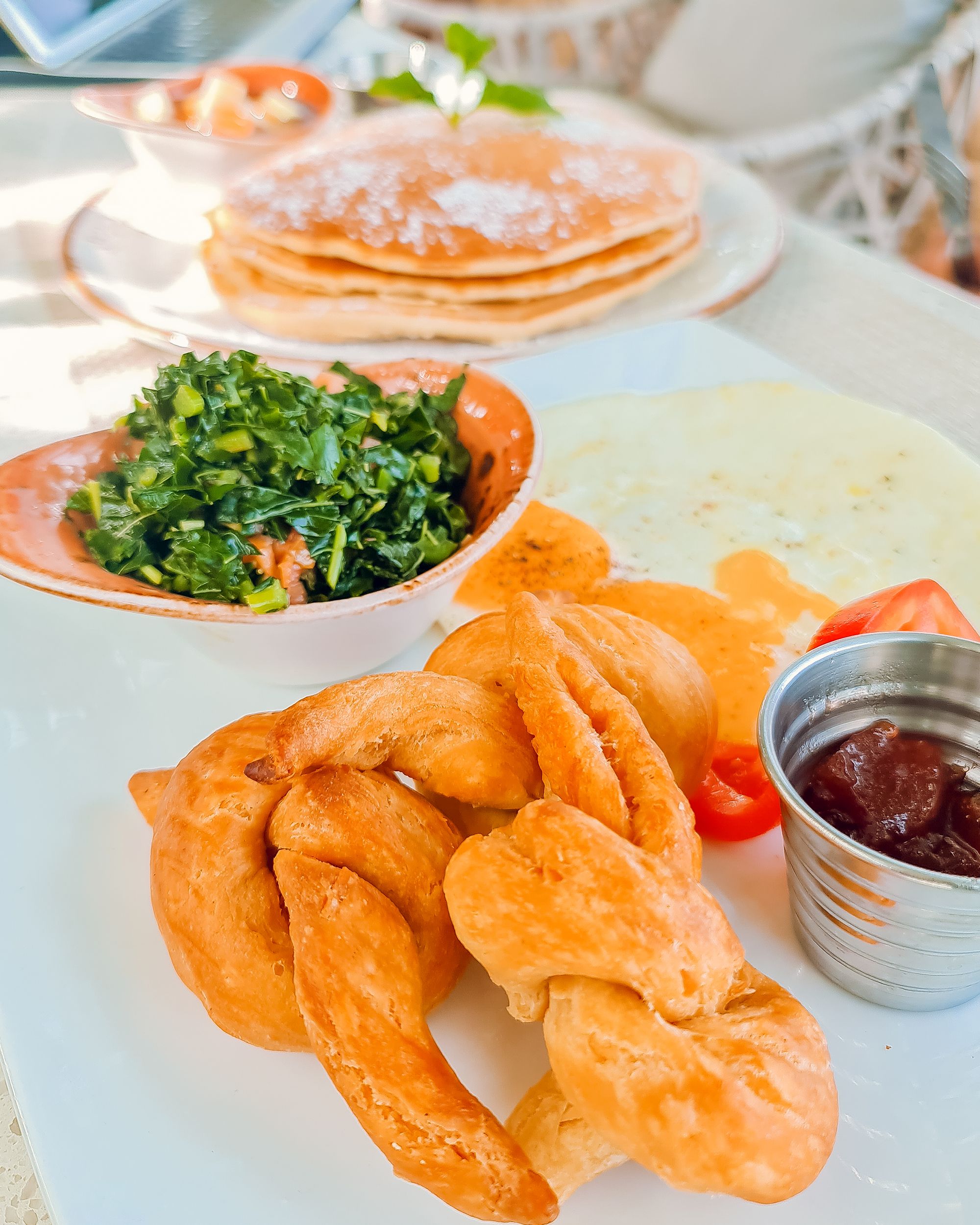 Golden fried chicken strips with a spinach side, maple syrup-dipped pancakes in the background, and a dollop of honey mustard on the side, deliciously plated.