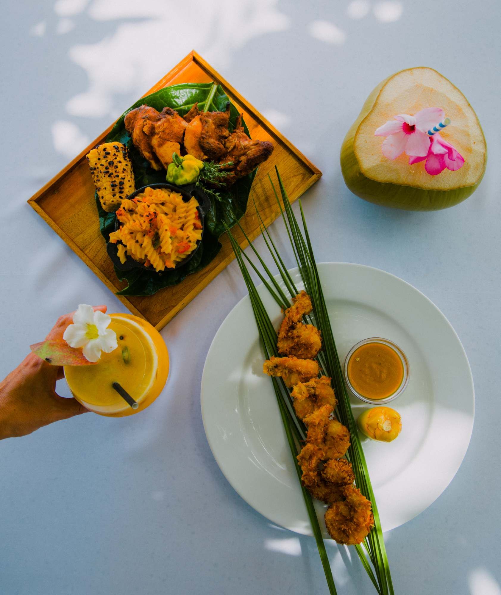 A vibrant spread of fried skewers and tempura on a plate with lime, dipping sauce, a tropical drink with a flower, and a carved lime garnish.
