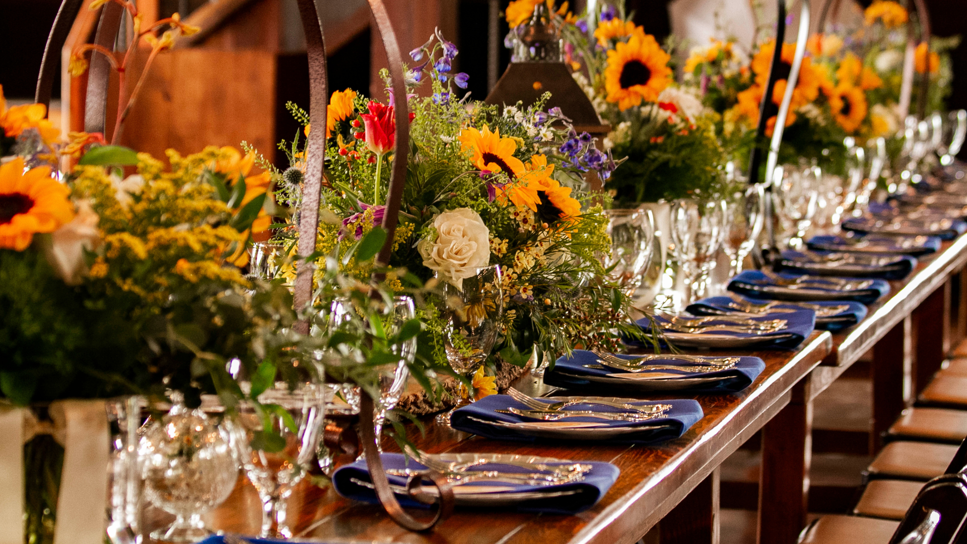 A long dining table set for a formal feast with colorful flower centerpieces, folded napkins, and glassware—elegant and festive.