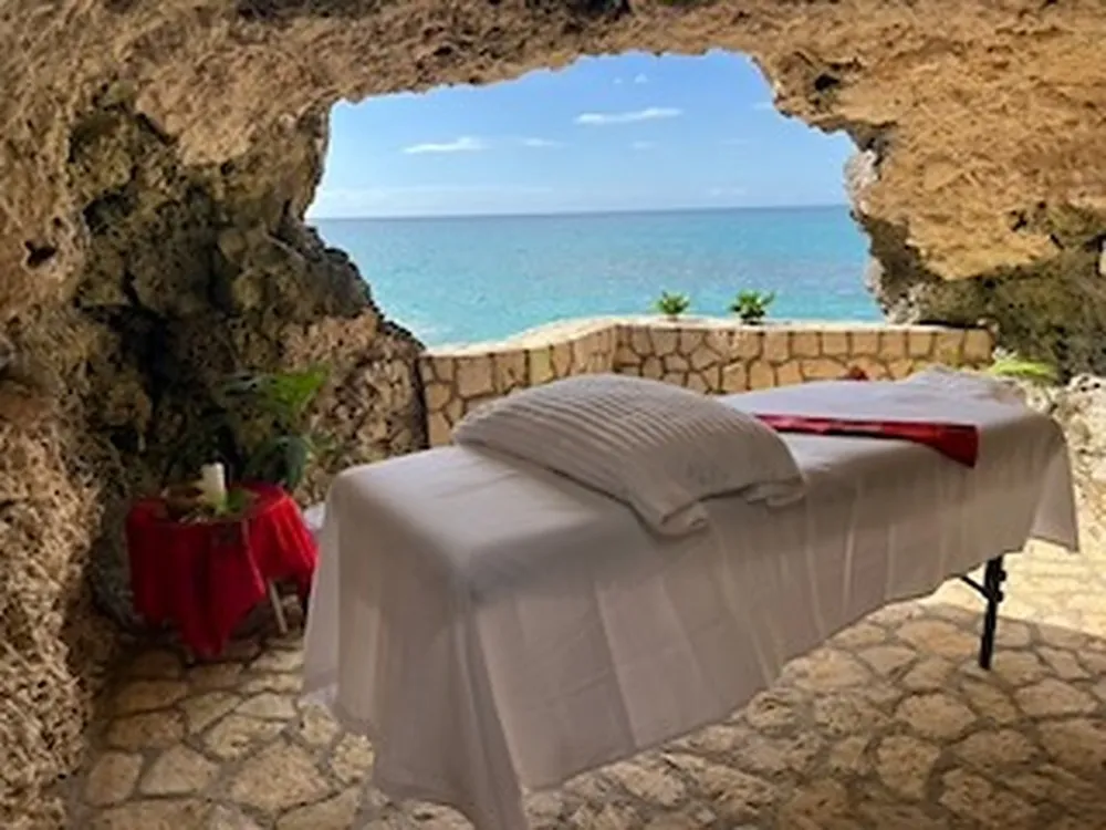 A massage table set inside The Cave by daylight, with the turquoise sea visible through the cave mouth.
